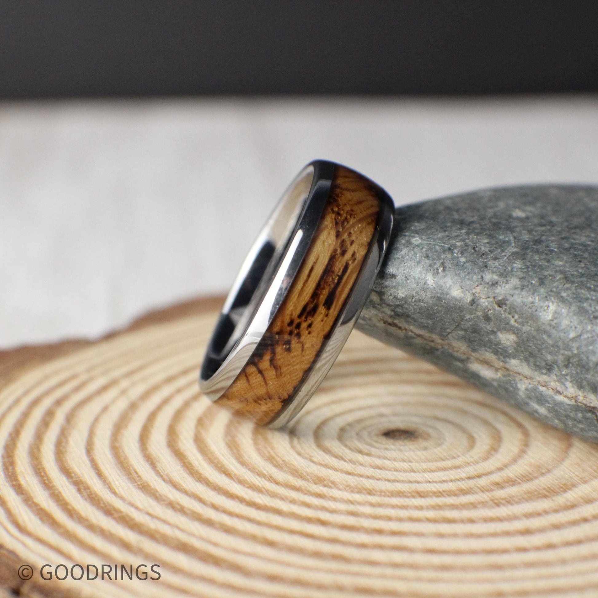 Domed profile tungsten ring resting on a woodgrain surface, showing off the warm whiskey barrel inlay. This 8mm men’s ring has a comfort-fit interior and polished exterior, combining strength, sentiment, and style in one rustic band.