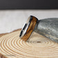 Domed profile tungsten ring resting on a woodgrain surface, showing off the warm whiskey barrel inlay. This 8mm men’s ring has a comfort-fit interior and polished exterior, combining strength, sentiment, and style in one rustic band.