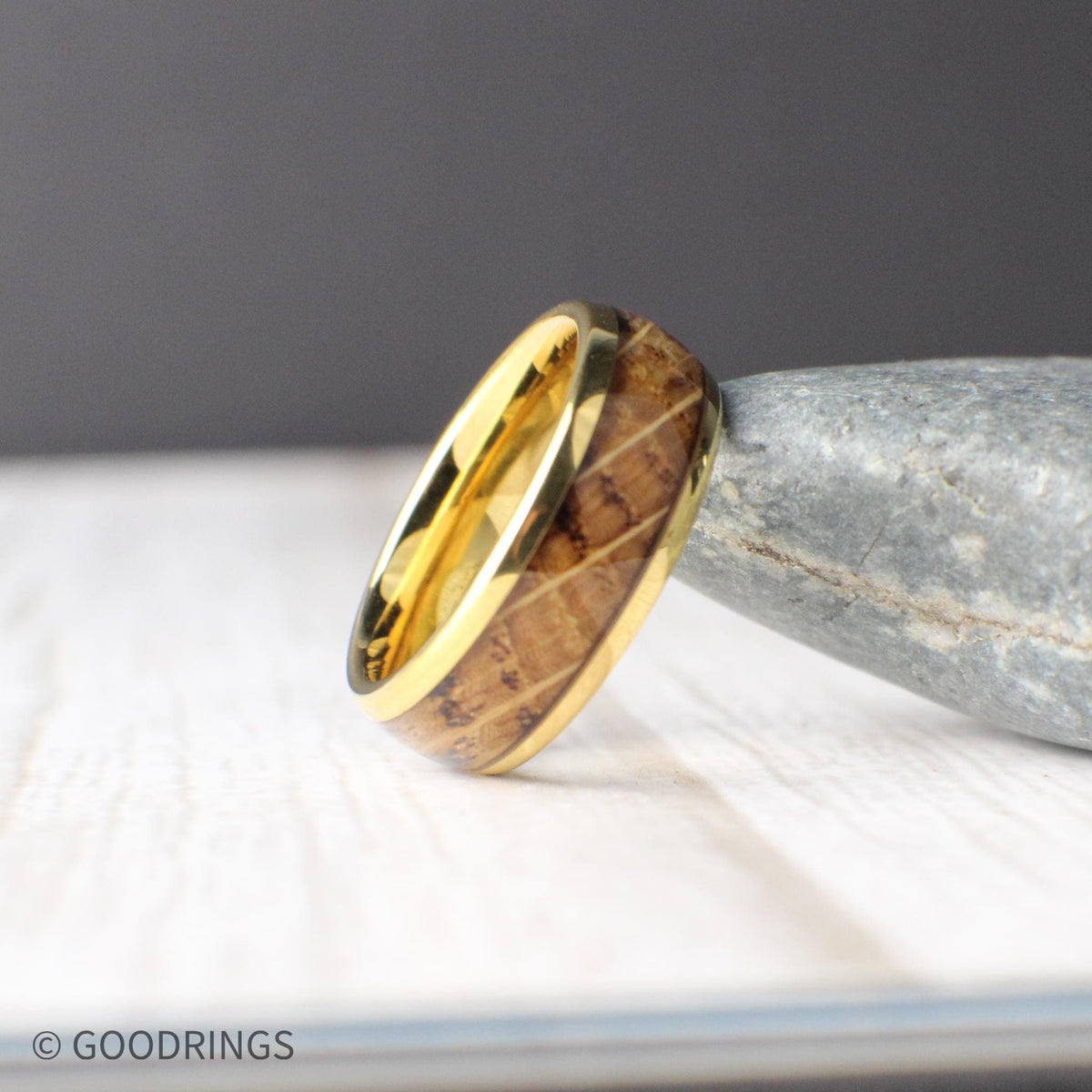 Shown resting on a smooth stone, this whiskey-inspired men’s ring has a polished gold-plated tungsten body with a real wood inlay. The domed profile provides a comfortable fit and timeless silhouette that’s perfect for weddings or whiskey-themed gifts.