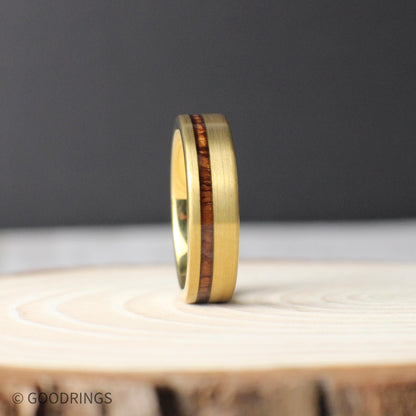 Standing upright on a wooden slab, this 6mm men’s tungsten ring showcases its offset inlay of Hawaiian Koa wood. The polished gold interior and brushed exterior reflect light subtly, while the unique grain of the Koa adds warmth and character.