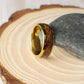Close-up view of a domed gold men’s ring made from tungsten and whiskey barrel wood. The 8mm band highlights the beauty of the reclaimed wood with natural textures and earthy hues, sealed in a high-gloss finish that protects and shines.