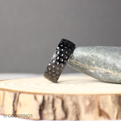 Close-up photo of an 8mm titanium ring with a golf ball inspired texture, featuring a sleek black finish and round dimples across the band, symbolizing strength, durability, and sporty style, perfect for golf lovers seeking a unique wedding band or promise ring that stands out with its bold design.