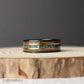 An 8mm wide men’s tungsten ring with a hammered black finish and a striking combination of moss agate, 18K rose gold, and whiskey barrel inlays. This band captures nature, craftsmanship, and sophistication in one design. The moss agate brings earthy greens, the rose gold adds sleek refinement, and the whiskey barrel wood represents rustic heritage. Ideal for weddings, anniversaries, or everyday wear.