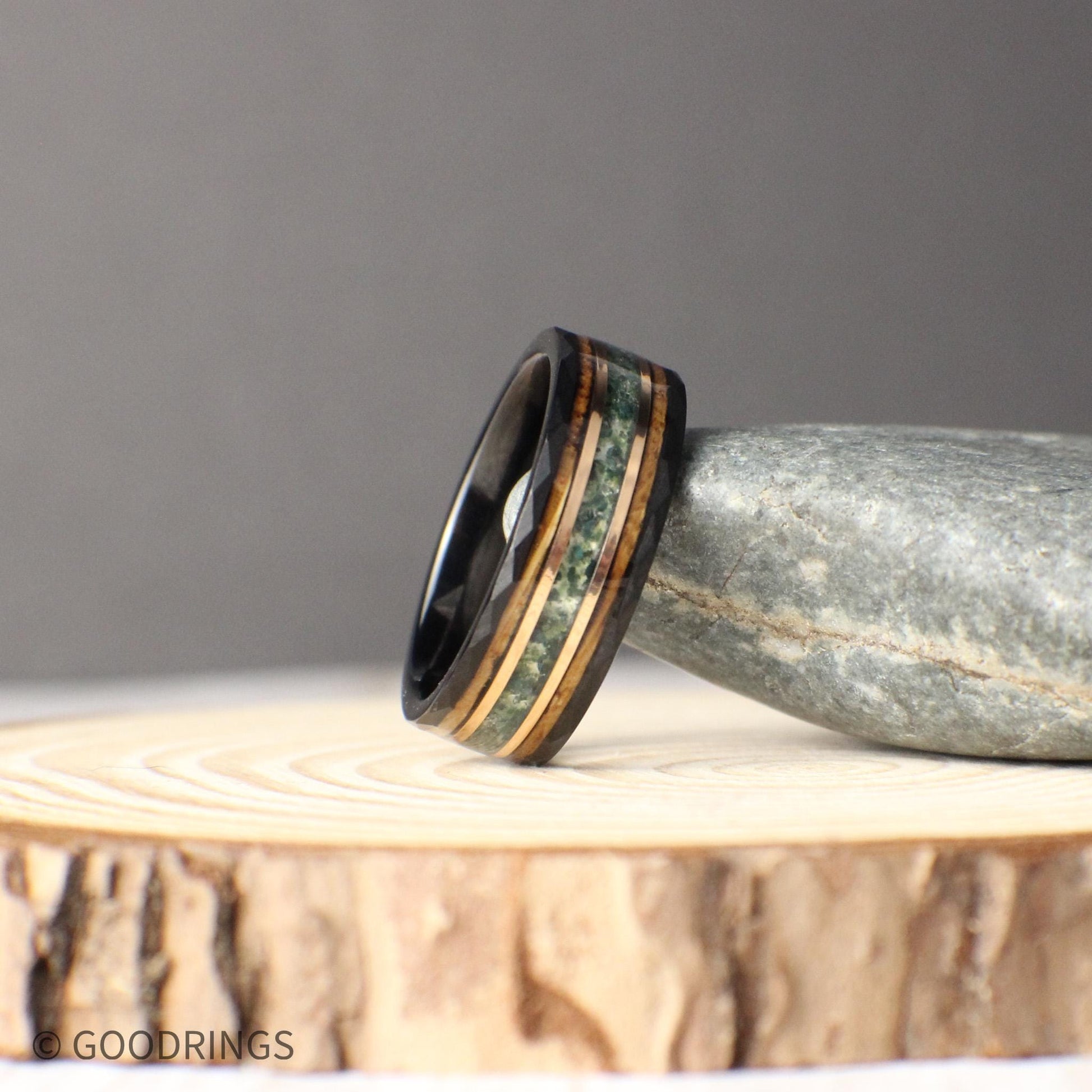 Black tungsten wedding band with 8mm width, showcasing inlays of moss agate, 18K rose gold, and whiskey barrel wood. The hammered black tungsten exterior is durable and modern, contrasted by the organic texture of moss agate, the glowing rose gold accent, and the rustic whiskey barrel finish. A unique, timeless ring design that symbolizes strength, history, and elegance for any special occasion.