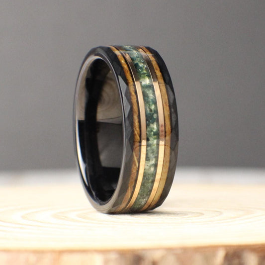 A bold 8mm black tungsten ring featuring a triple inlay of moss agate, 18K rose gold, and burnt whiskey barrel wood. The hammered tungsten band provides a rugged yet refined foundation, while the green moss agate adds natural vibrance, the rose gold line brings warmth, and the whiskey barrel wood offers a rustic character. Perfect as a wedding band, anniversary ring, or meaningful everyday piece.