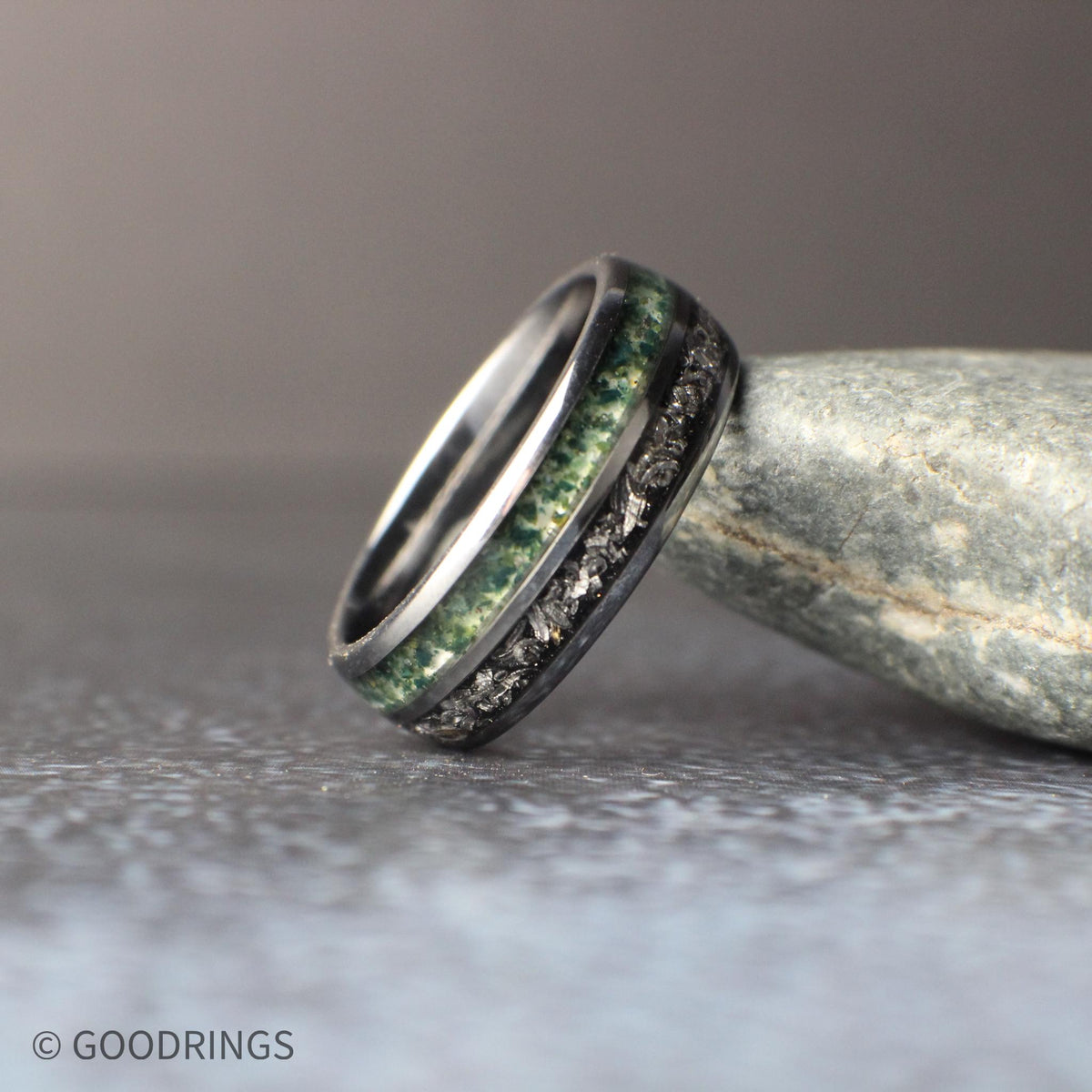 Matching his and hers tungsten wedding rings shown side by side. The 8mm ring features a bold combination of meteorite and moss agate inlays, while the slimmer 4mm ring showcases a clean moss agate inlay in a black core. The image emphasizes the contrast between organic stone textures and the sleek, durable tungsten design.