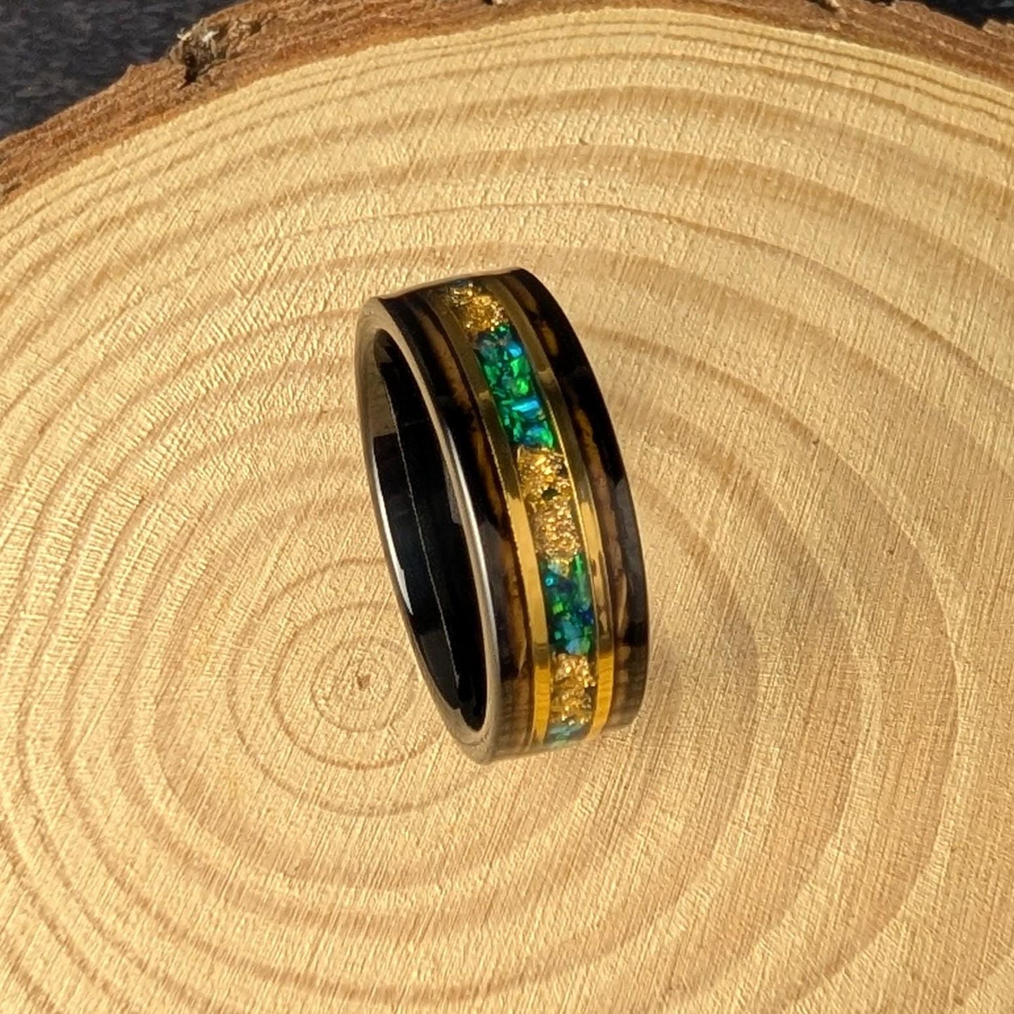 Side view of an 8mm tungsten ring showcasing layered green opals and gold detailing with a wood-lined interior