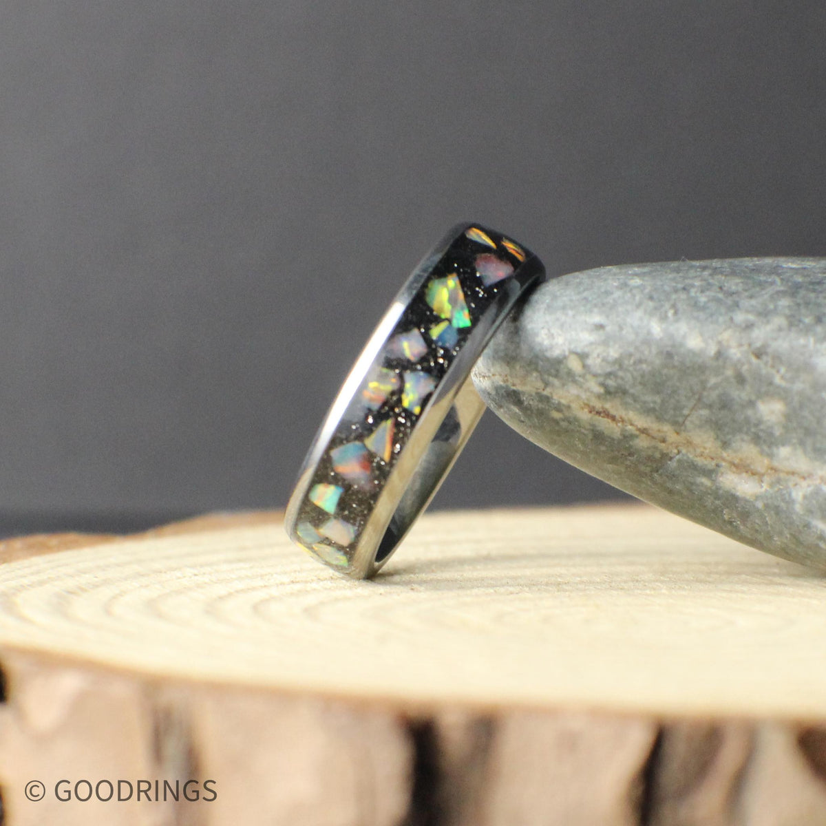 Two 6mm tungsten opal rings photographed together on a rustic wood background. Each ring shows unique opal patterns with flashes of green, blue, and warm tones, highlighting the individuality of every piece. The polished tungsten finish adds durability and a sleek, modern feel.