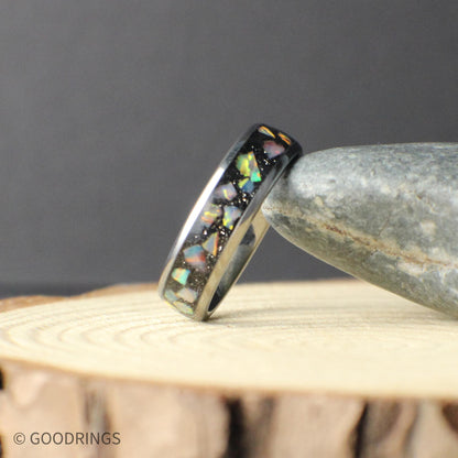 Two 6mm tungsten opal rings photographed together on a rustic wood background. Each ring shows unique opal patterns with flashes of green, blue, and warm tones, highlighting the individuality of every piece. The polished tungsten finish adds durability and a sleek, modern feel.