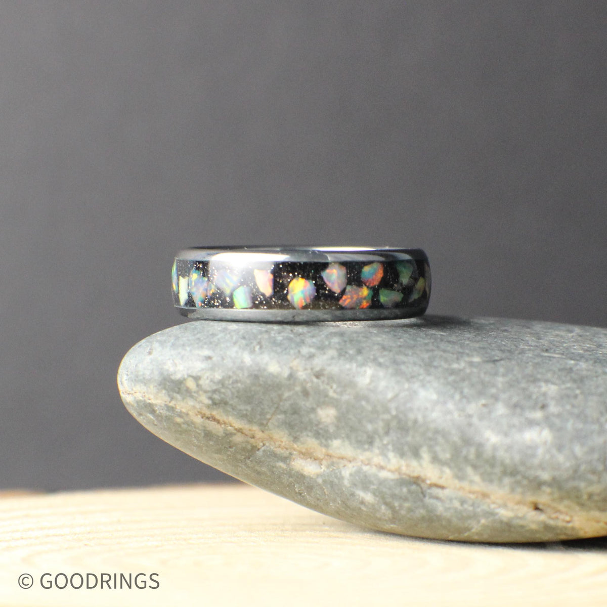 Angled close-up of a slim tungsten ring featuring a crushed opal inlay. The opal fragments sparkle against the dark band, creating depth and movement in the design. The narrow width and smooth finish make this ring an ideal choice for those who prefer a lighter, low-profile wedding band.
