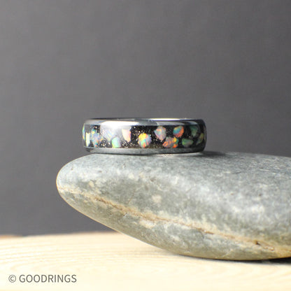Angled close-up of a slim tungsten ring featuring a crushed opal inlay. The opal fragments sparkle against the dark band, creating depth and movement in the design. The narrow width and smooth finish make this ring an ideal choice for those who prefer a lighter, low-profile wedding band.