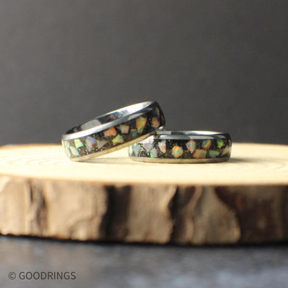 Close-up of a 6mm tungsten opal ring resting on a natural wood surface. The polished tungsten band features a crushed opal inlay with flashes of green, blue, and orange that shimmer against the dark background. The slim profile highlights the modern design, making it ideal for a wedding band or everyday ring with a subtle pop of color.
