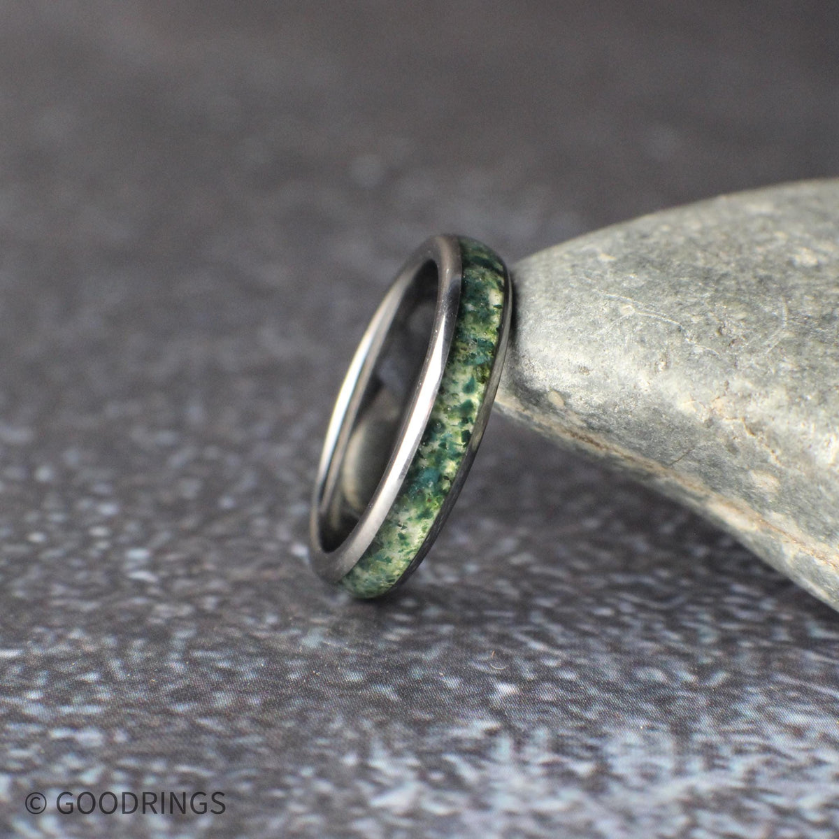 Couples matching wedding bands made from black tungsten. The men’s 8mm ring features a striking meteorite and moss agate inlay combination, while the women’s 4mm ring offers a refined moss agate inlay for a simpler look. The photo highlights the balance between bold texture and understated elegance in this nature-inspired ring set.