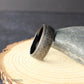 Detailed macro photo showing the etched texture of the tribal pattern on a black tungsten wedding band. The engraved sections reveal a brushed silver gray tone that contrasts against the polished black interior.