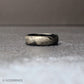 Detailed macro view of a 6mm comfort fit black tungsten band engraved with flowing feather artwork around the entire circumference of the ring.