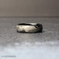 Nature-inspired 6mm black tungsten wedding band featuring an intricate feather design etched in silver tone, photographed in soft natural lighting.