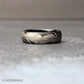 6mm black tungsten ring with a continuous silver feather engraving wrapped fully around the band, shown resting on a textured gray surface with a clean, minimal background.