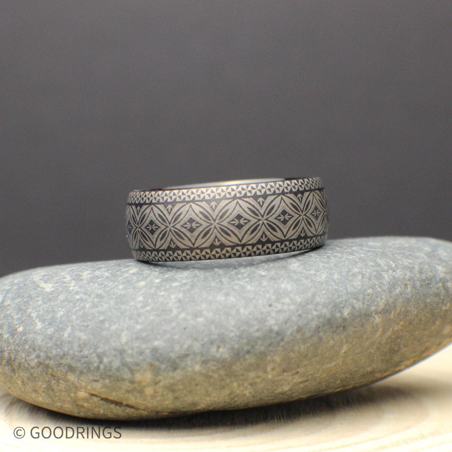 Side view of a black tungsten carbide wedding ring with comfort fit interior and wrap around tribal engraving. The silver colored etched pattern stands out clearly against the dark finish giving a masculine but refined appearance.