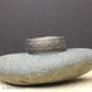 Side view of a black tungsten carbide wedding ring with comfort fit interior and wrap around tribal engraving. The silver colored etched pattern stands out clearly against the dark finish giving a masculine but refined appearance.
