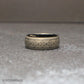 Close up of a black tungsten ring featuring a continuous Polynesian tribal engraving pattern wrapping around the entire band. The silver gray etched design contrasts against the dark metal creating a bold mens wedding band photographed on natural wood.