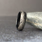Close-up side angle of a black tungsten feather ring leaning against a smooth stone, highlighting the detailed silver engraved feather pattern and polished comfort fit interior.