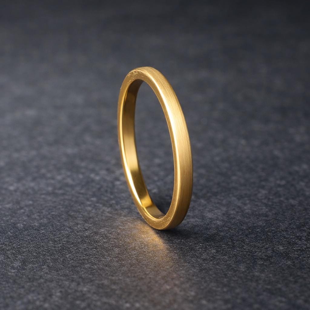 Slim gold tungsten wedding band standing upright on a dark stone-textured surface, showcasing a brushed matte exterior and polished interior. The clean, minimalist design emphasizes a modern and timeless look, perfect as a men’s or women’s wedding band. The soft lighting highlights the warm gold tone and smooth comfort fit profile.