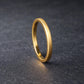 Slim gold tungsten wedding band standing upright on a dark stone-textured surface, showcasing a brushed matte exterior and polished interior. The clean, minimalist design emphasizes a modern and timeless look, perfect as a men’s or women’s wedding band. The soft lighting highlights the warm gold tone and smooth comfort fit profile.