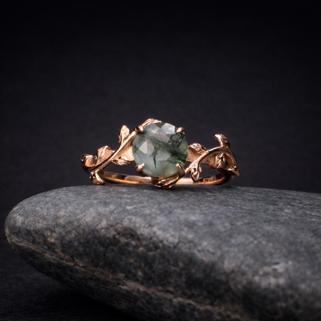 Moss agate wedding ring on a rock. The ring is 18K rose gold and it has leafs in the design.