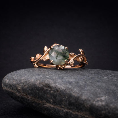Moss agate wedding ring on a rock. The ring is 18K rose gold and it has leafs in the design.