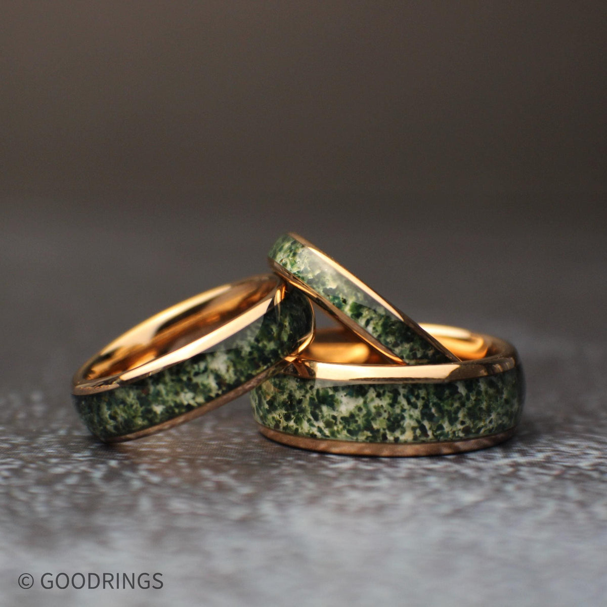 three moss agate rings in different widths on a dark background. The rings are 4mm, 6mm, and 8mm wide.