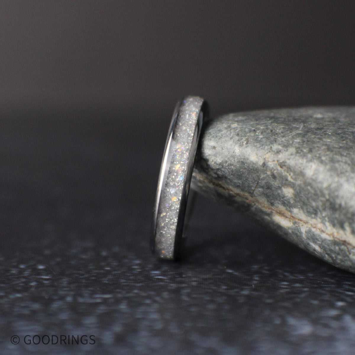 side profile of thin moonstone ring showing polished edges and sparkling crushed inlay on dark textured surface