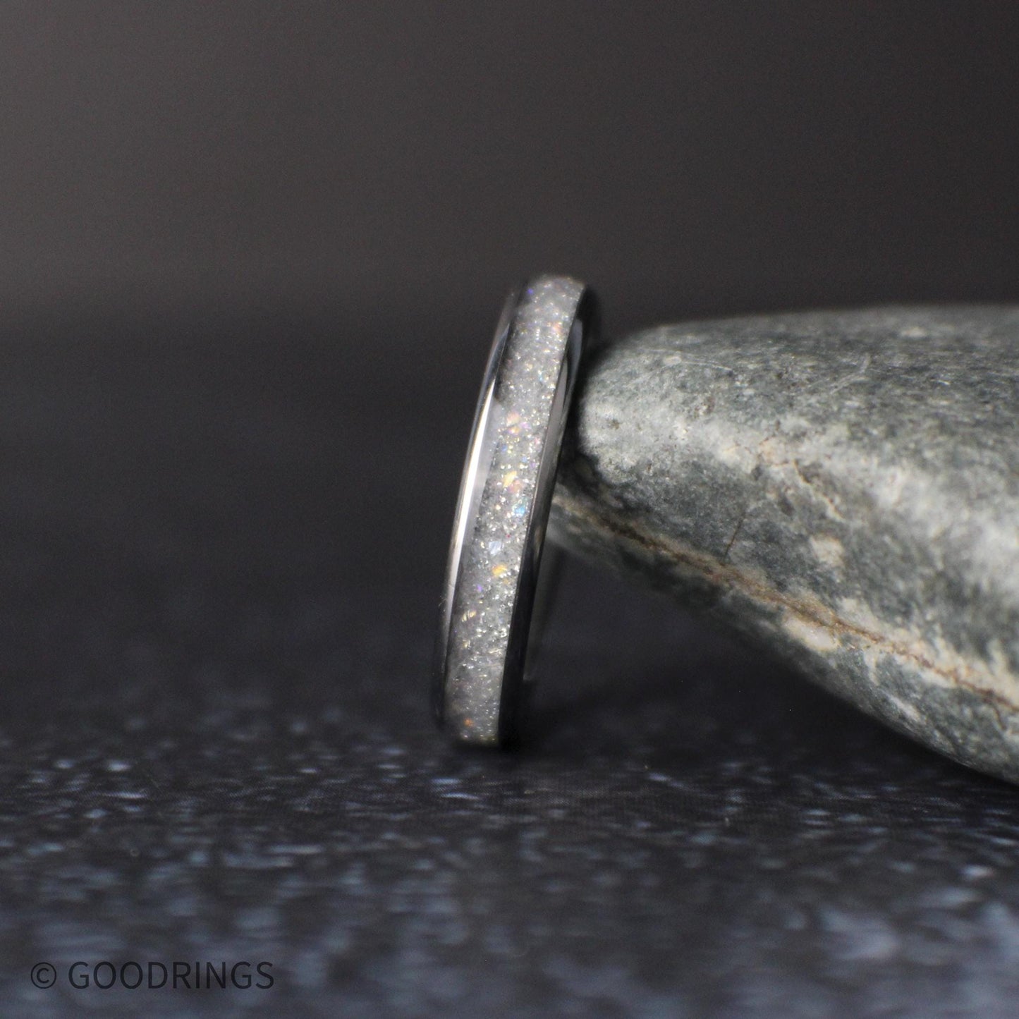 side profile of thin moonstone ring showing polished edges and sparkling crushed inlay on dark textured surface