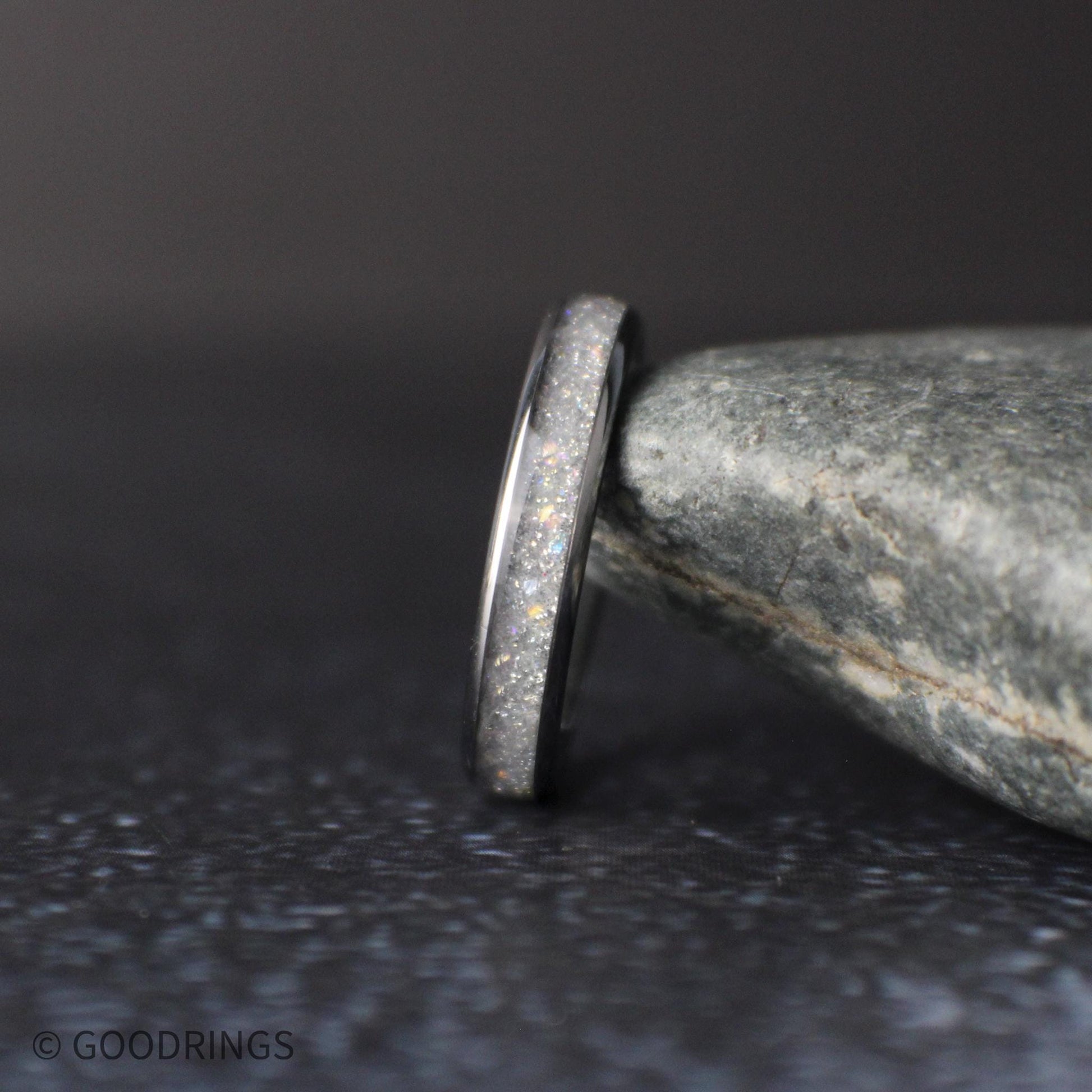 side profile of thin moonstone ring showing polished edges and sparkling crushed inlay on dark textured surface