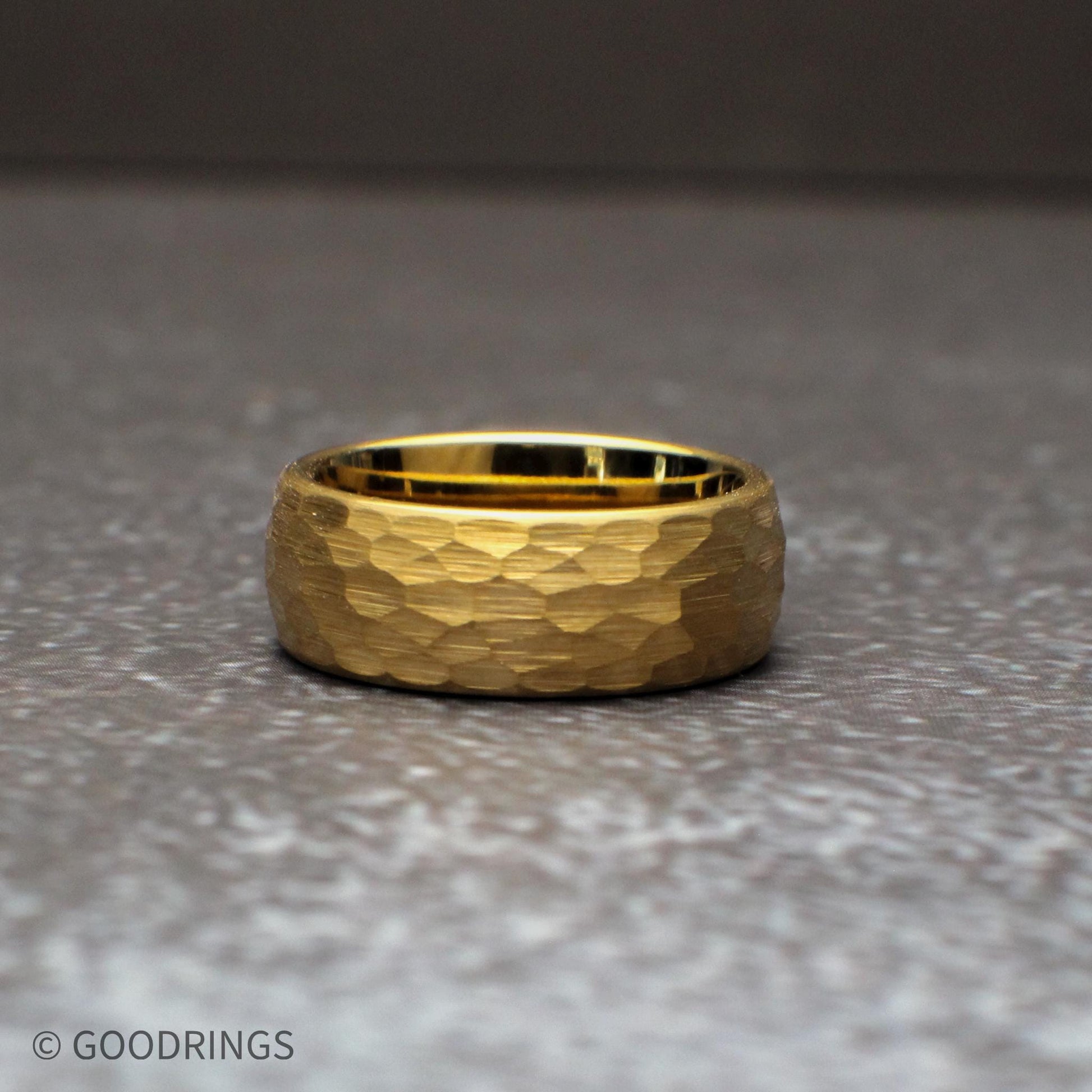 Bold 8mm hammered gold tungsten ring designed for a strong, statement look. The wide band and hammered texture reflect light across the surface, creating a rugged yet refined appearance, ideal for men’s wedding bands or those who prefer a more substantial gold ring.