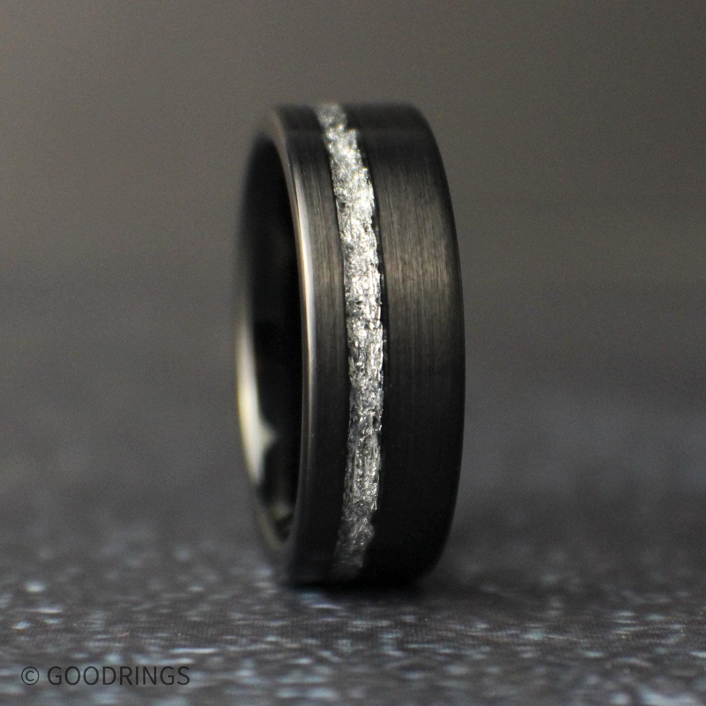 Close-up of a black tungsten wedding ring with textured genuine silver leaf inlay and modern brushed black finish.
