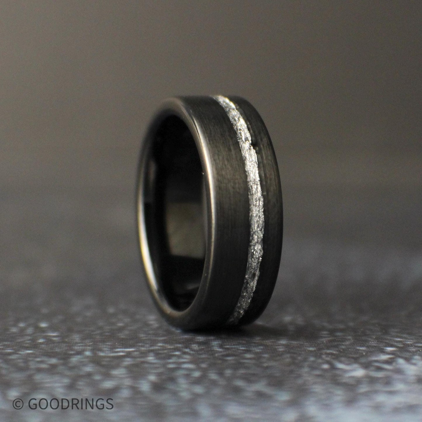 Black tungsten men’s wedding band with an offset silver leaf channel, brushed matte finish, and rounded comfort fit edges.