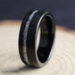 Men’s black tungsten ring featuring a brushed finish and offset silver leaf inlay, displayed upright on natural wood.