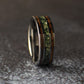 Close angled view of the moss agate and whiskey barrel wood tungsten ring leaning against a gray stone on a dark textured background.