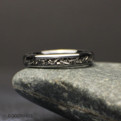 Front view of the slim polished tungsten band resting horizontally on a gray stone, with meteorite shavings visible across the dark center inlay.