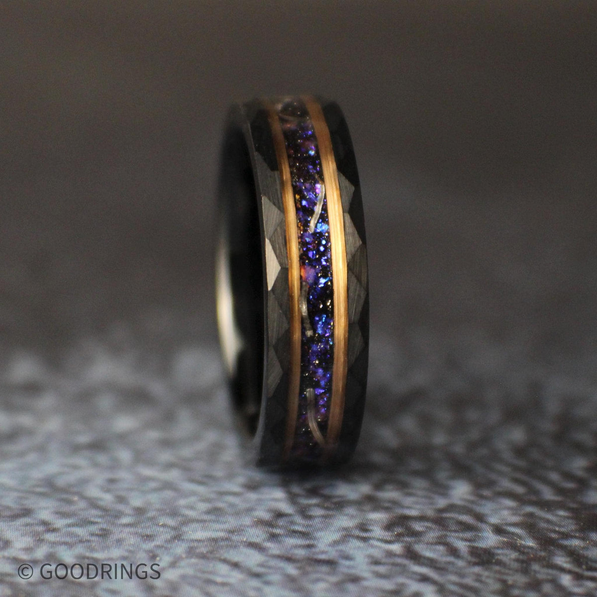 Three-quarter view of a 6mm black tungsten ring standing upright, with faceted edges, rose-gold accents, and a purple-blue galaxy inlay containing meteorite shavings.