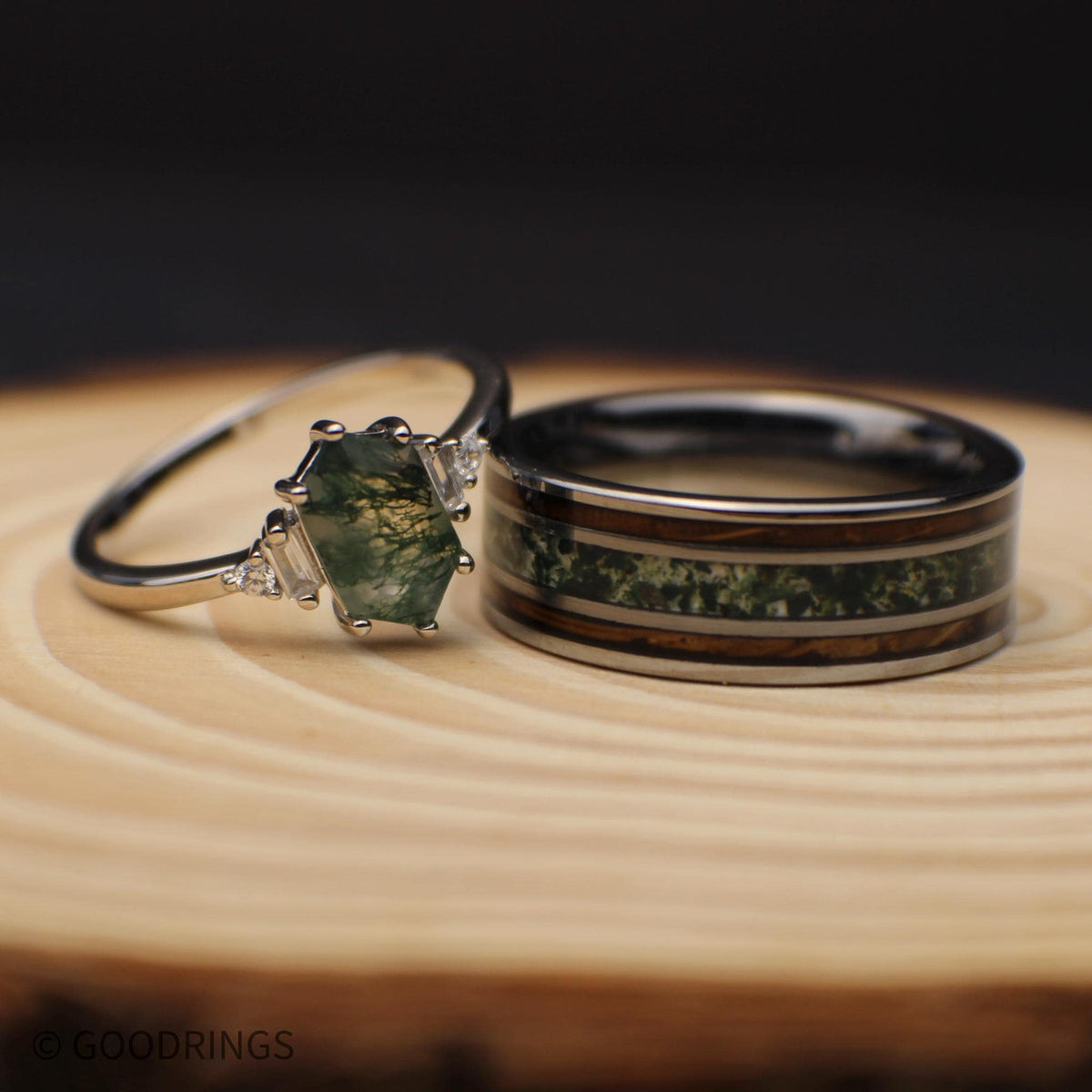 Close view of a sterling silver moss agate engagement ring beside an 8mm tungsten band with green moss agate and two brown wood inlays.