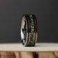 Elevated front view of the gunmetal tungsten band lying flat, showing its polished comfort-fit interior, green moss agate center, and whiskey barrel wood inlays.