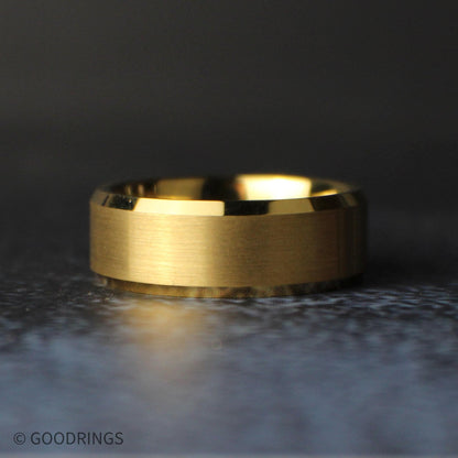 Low angled view of the gold tungsten ring lying on its side, showing the wide brushed center, reflective beveled edges, and polished interior.