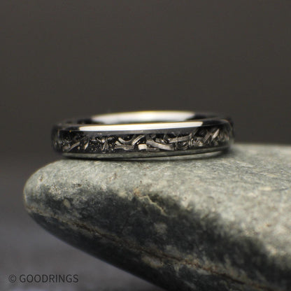 Three-quarter view of the polished tungsten wedding band standing beside a gray stone, highlighting its narrow meteorite shaving inlay.