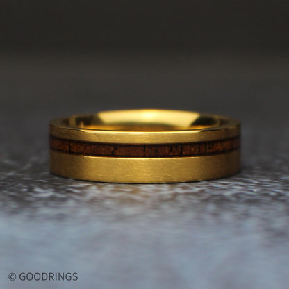 Straight front view of the 6mm gold titanium wedding band lying horizontally, with a narrow koa wood inlay positioned above the center of the brushed band.