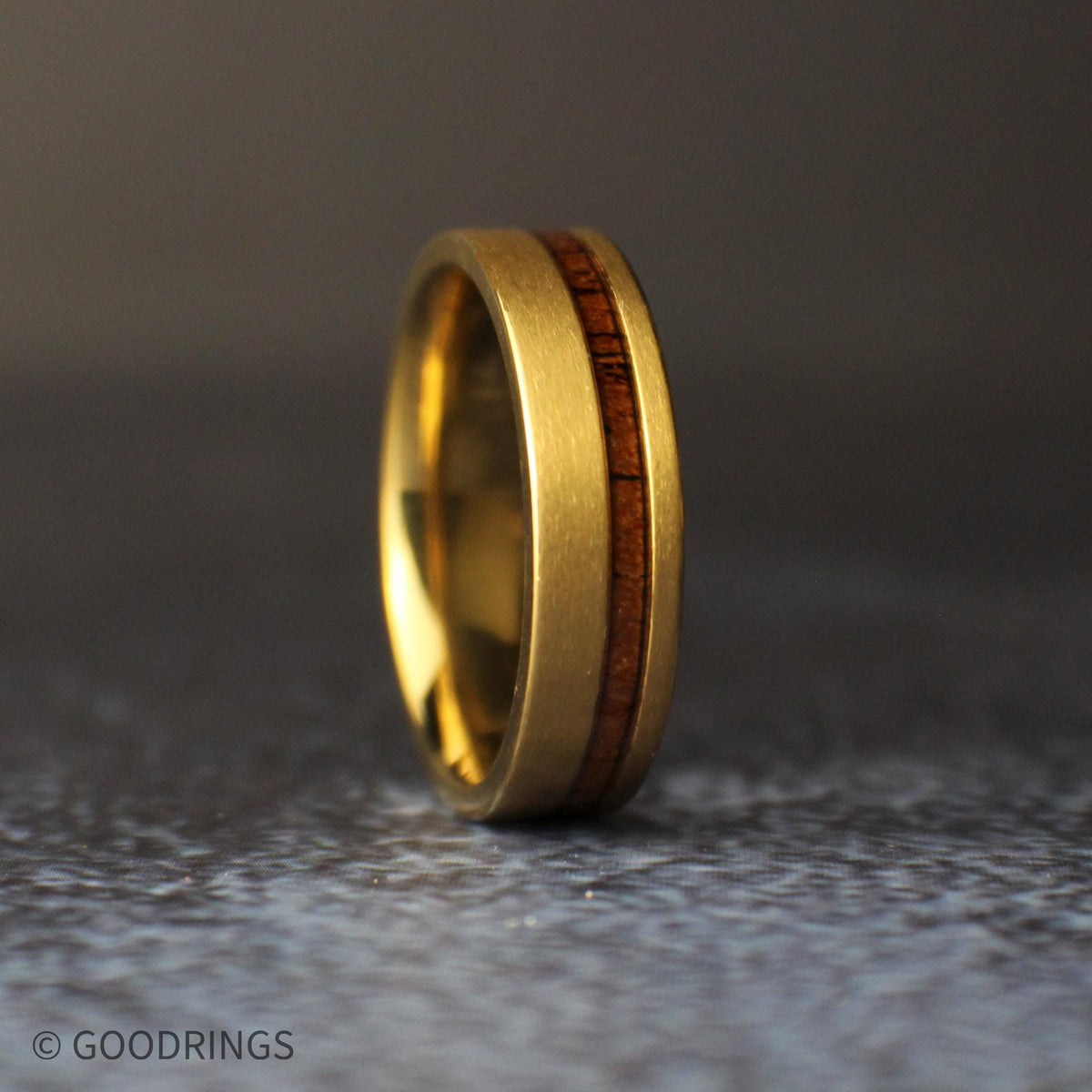 Straight front view of the 6mm brushed gold titanium ring standing upright, displaying the grain and asymmetrical placement of its koa wood inlay.