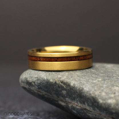 Angled view of the lightweight gold titanium wedding band standing on a dark surface, with a warm brown koa wood stripe set off center.