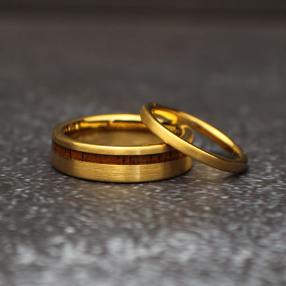 Angled view of the couples tungsten ring set, showing the narrow brushed gold band resting across the wider gold and koa wood wedding band.