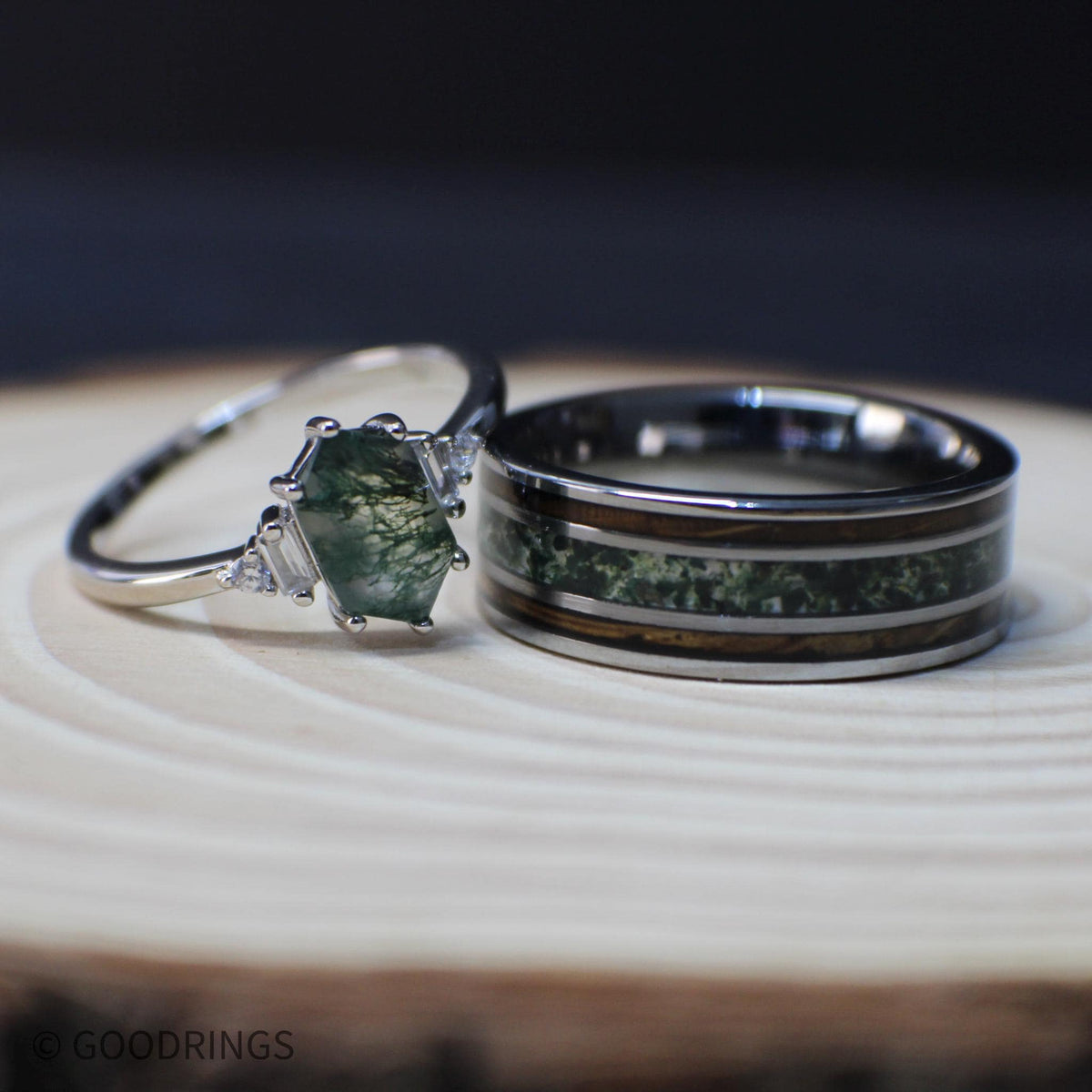 Coordinated moss agate couples rings resting on a light wood surface, showing the patterned center stone and crushed green inlay side by side.