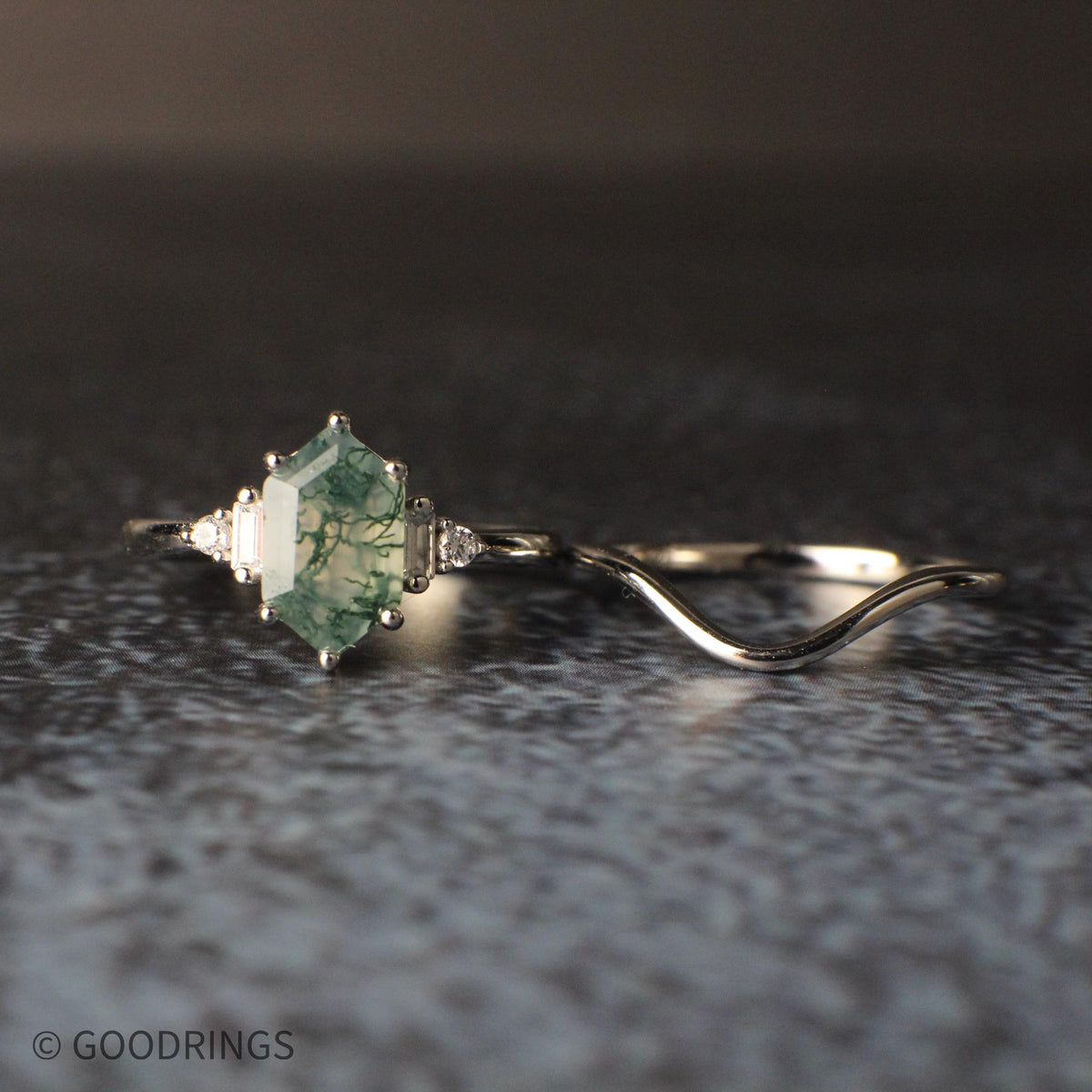 Female moss agate stone setting ring with bridal set laying next to it on dark background